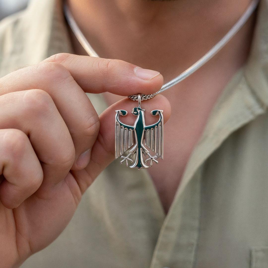 Ein Mann hält den Adler Anhäger der Deutschland Kette zwischen Daumen und Zeigefinger